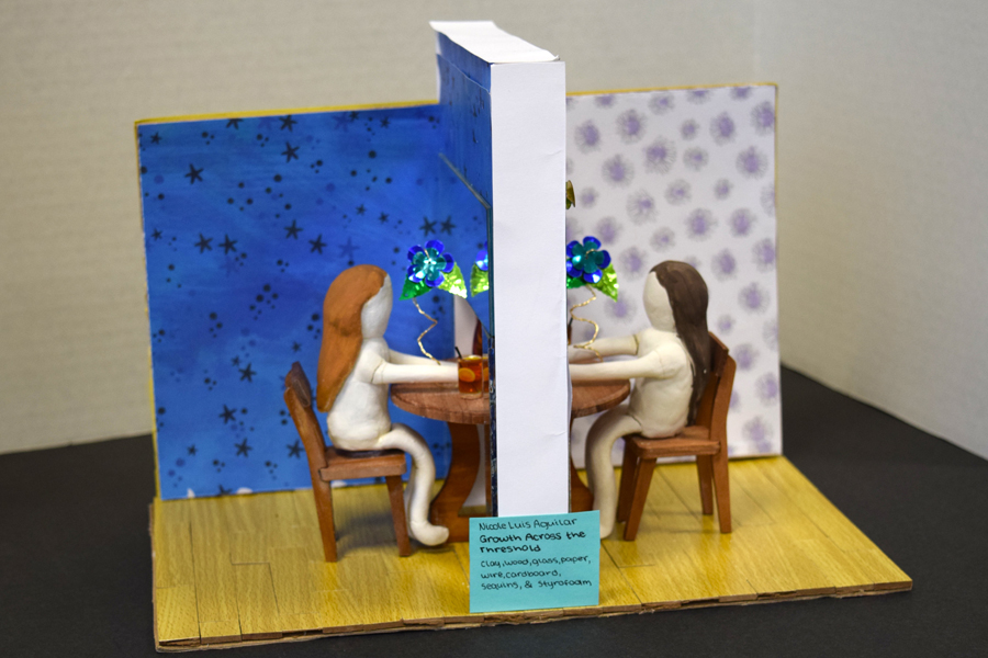 Twi clay figures sitting at a table looking at each other behind a wall