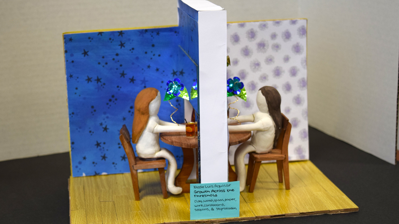 Two clay figures sitting at a table looking at each other behind a wall