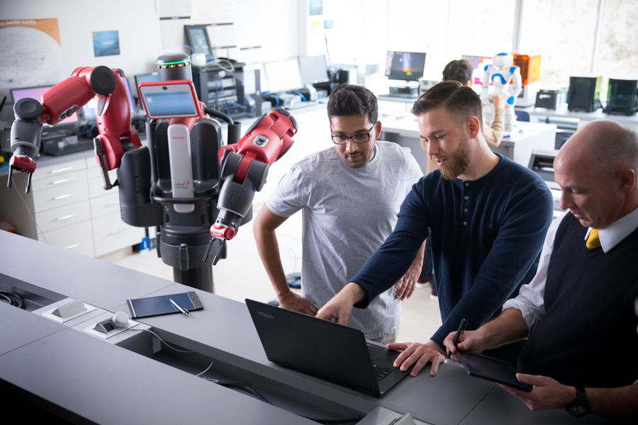 Two students and a professor are working in the Entrepreneurship & Technology Innovation Center with a red robot pictured.