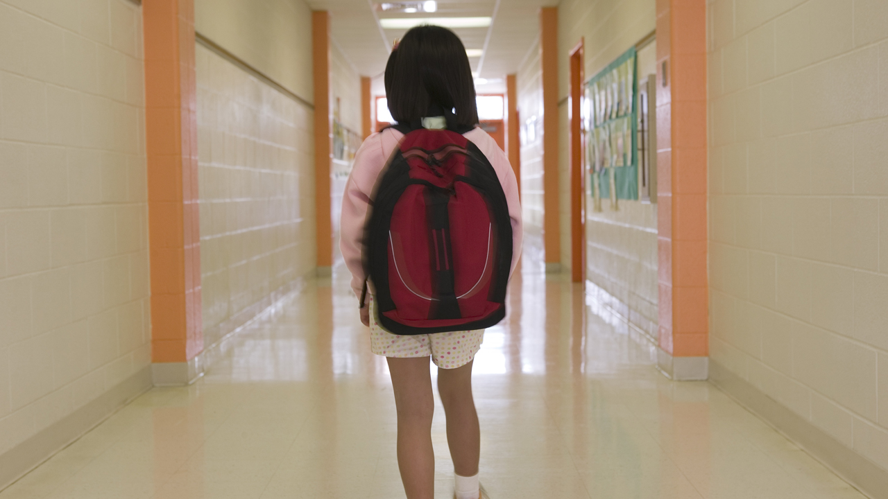 Young child carrying backpack walking in school hallway