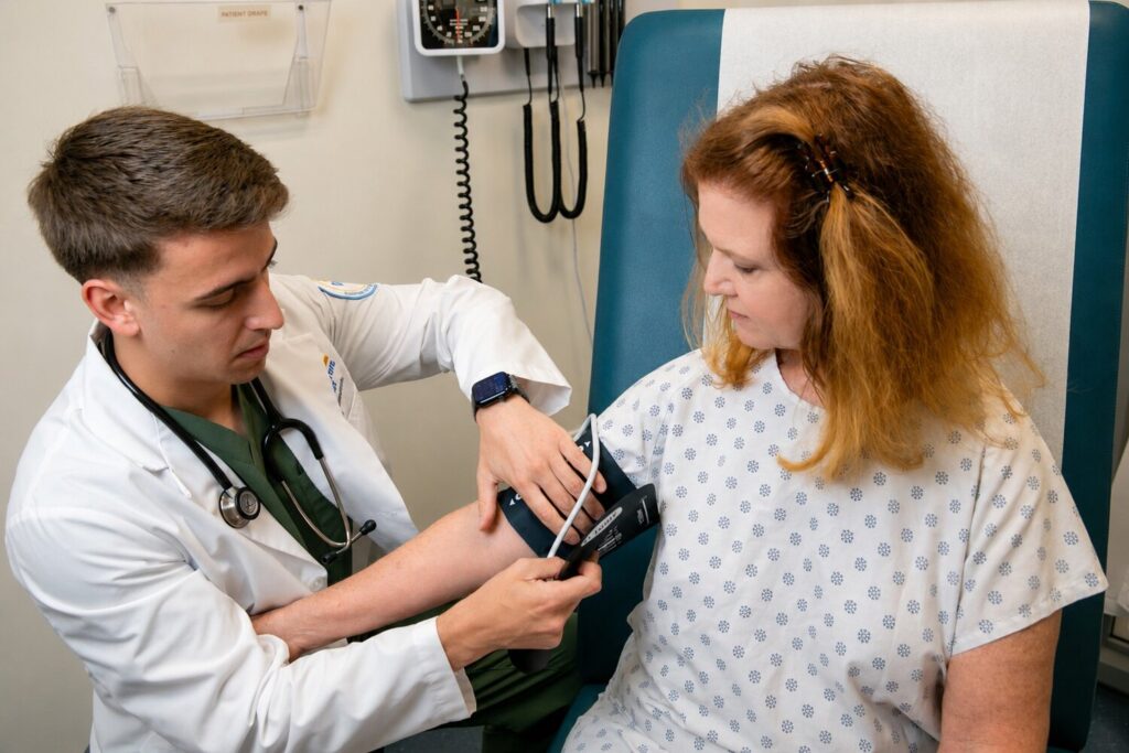 Medical student taking the blood pressure of a standardized patient in an exam room