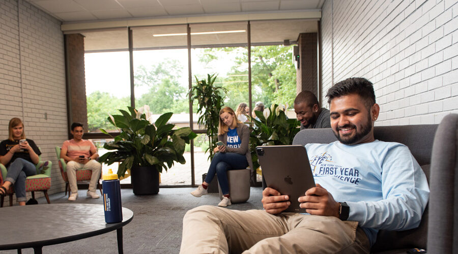 A group of first-year New York Tech students sits in a common area to review information on their smartphones or tablets.
