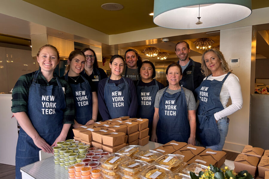 Group of New York Tech staff wearing aprons standing in front of boxes of food
