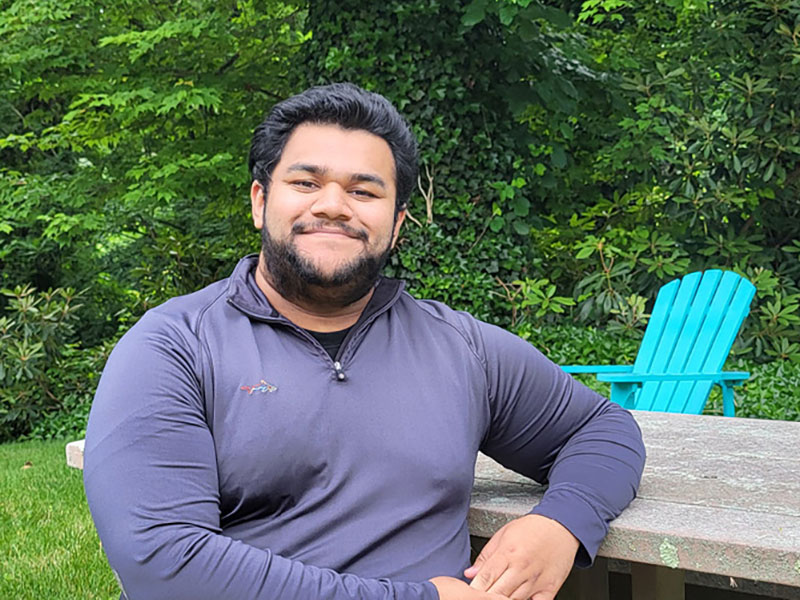 A student in a blue shirt sits outside on a bench at New York Tech's Long Island campus.