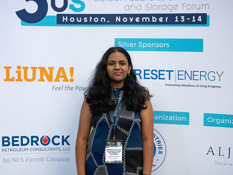 New York Tech student standing confidently in front of a banner at a conference.